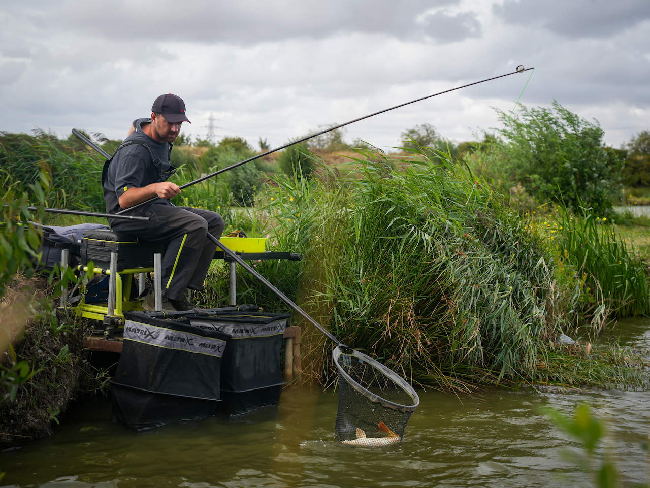 Man sitting on seatbox catching fish in net