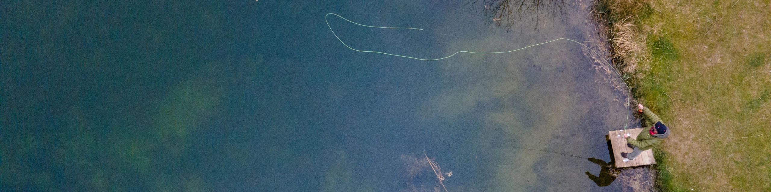 Angler stood on bank casting a fishing rod, viewed from above